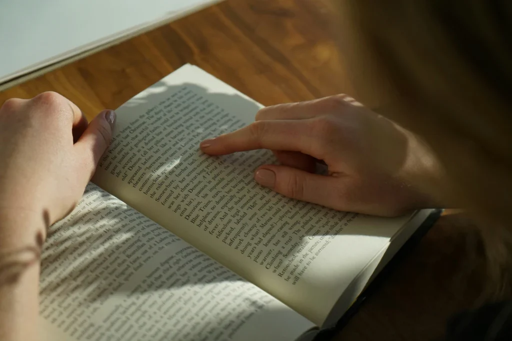 Over the shoulder shot of a woman reading a book laid flat on a desk